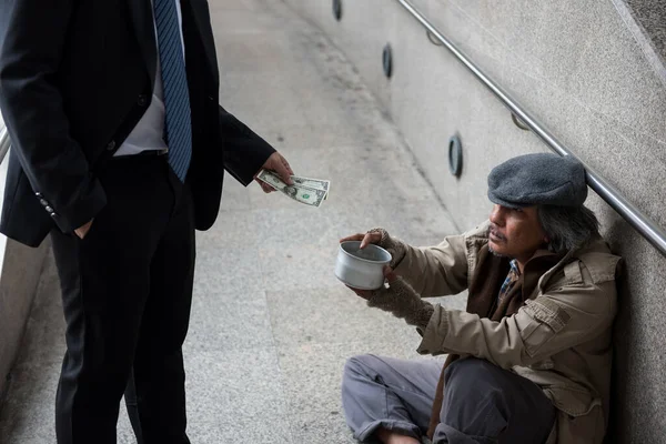 親切なビジネスマンは2ドル札を都市の町の歩く古い乞食かホームレスの人に与える 貧困と社会問題の概念 Covid 19オミクロンパンデミックの間に分かち合いを与える — ストック写真
