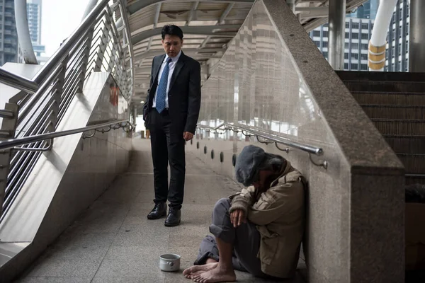 黒のスーツを着た親切なビジネスマンは 都会の街を歩く老人やホームレスを見ています 貧困と社会問題 — ストック写真