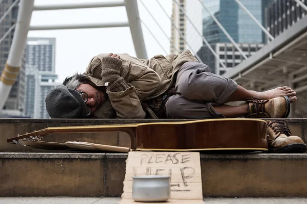 古い乞食やホームレスの男性はギターで近代的な都市の階段で寝て ボウルを寄付し ヘルプテキストと紙の段ボール 悪天候の冬は寒さを感じ — ストック写真