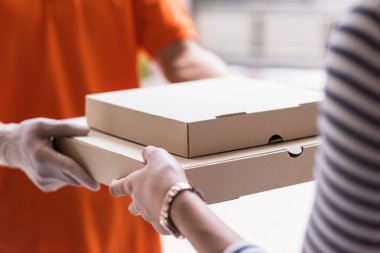 Pizza teslimatı. Müşterinin yakın elleri, ornage üniformalı teslimatçıdan yiyecek teslimatı alıyor. Covid-19 omicron salgınını önlemek için mobil uygulama ile yeni normal kurye yemek servisi.