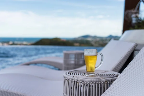 Glass of ice cold beer by swimming pool with blur sea view,  Hua Hin, Thailand.  Summer holiday maker or vacation in tropical country, Siam.