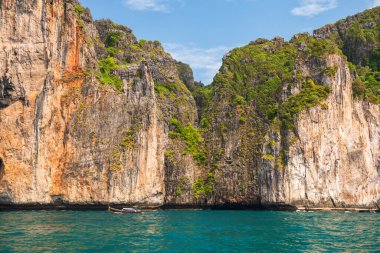 Tourist wooden boat sailing on crystal water with beautiful karst mountain near Monkey bay at Phi Phi island, Krabi, Thailand. Famous travel destination or summer holiday vacation in Siam.