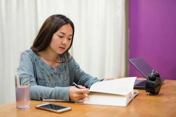 University Asian girl reading text book for final exam preparation in the living room at home.