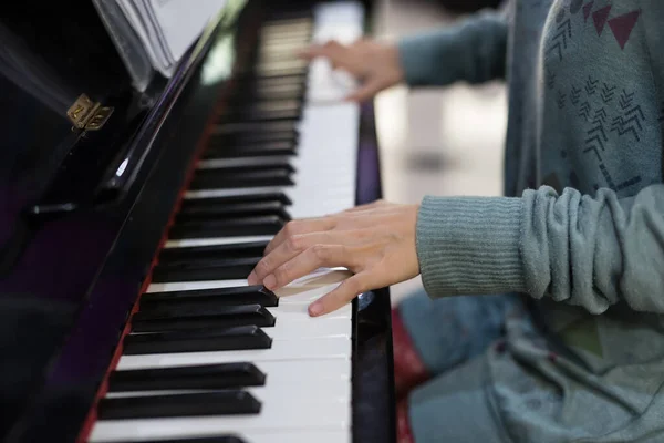 Young woman playing piano at home, closeup fingers of left hand in sweater.