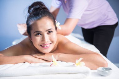 Asya 'dan gülümseyen güzel bir kadın Tayland yağlı sırt masajı ve beyaz Plumeria ile kaplıca salonu. Masözün vücut bakımı uygulaması. Alternatif sağlık sektörü