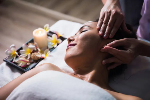 Thai oil Ayurvedic face and ear massage on bed to Asian woman by professional masseuse. Anti-aging facial treatment in spa salon. Girl with alternative medicine therapy.