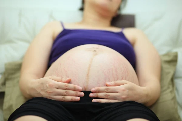 pregnant woman lying relax on bed and touching her 36 weeks belly by hands