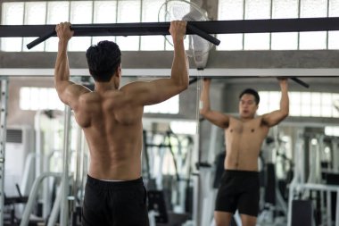 Muscular Asian man pulling up on horizontal bar in gym