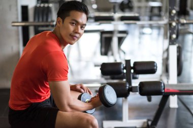 Portrait of smiling Asian fit man hold heavy dumbbells in fitness gym. Muscular body sportsman. Bodybuilding and healthy sport lifestyle concept.