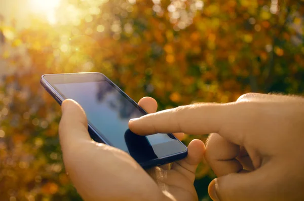 Erkek ellerini kullanan bir akıllı telefon, doğa arka plan closeup. — Stok fotoğraf