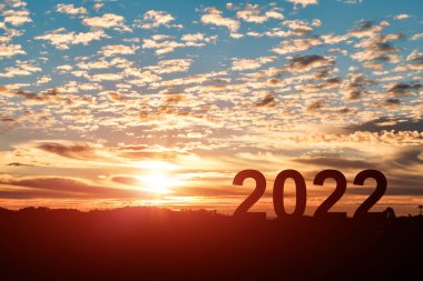 Yeni yıl kavramı 2022. 2021 'den 2022' ye, bulutlu gökyüzü günbatımı arka planıyla atlayan insan silueti..