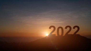 Mutlu yıllar 2022. Dağdaki harflerin silueti güzel bir gün batımı ya da gün doğumu gökyüzü ve bulutlar.