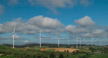 Çevre gücü, tepeli manzara ve mavi gökyüzü arka planında rüzgar türbini alanı.