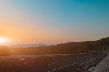 Asfalt yolu ve dağ manzarası günbatımında gökyüzü arka planında. Kırsal yol ve dağlar.