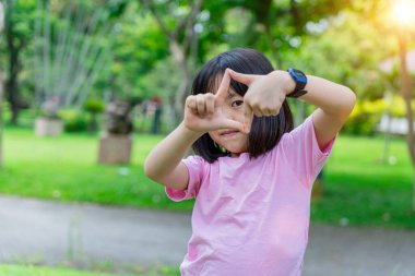 Gülümseyen kız çocuğu, elleri ve parmaklarıyla çerçeve yapıyor. Yaratıcılık ve fotoğrafçılık kavramı.