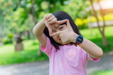 Gülümseyen kız çocuğu, elleri ve parmaklarıyla çerçeve yapıyor. Yaratıcılık ve fotoğrafçılık kavramı.