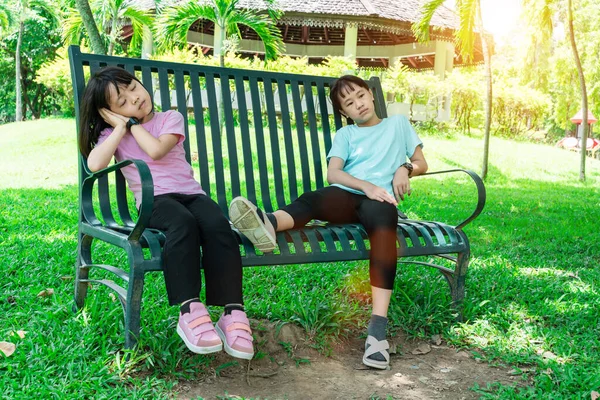 两个姐姐坐在一个绿色公园的长椅上 — 图库照片
