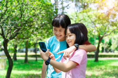 Parkta cep telefonu kullanırken sarılan iki kız kardeş. Mutlu aile kavramı.