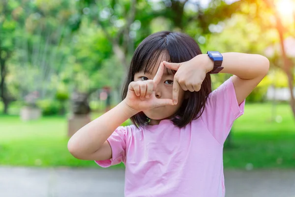 Gülümseyen kız çocuğu, elleri ve parmaklarıyla çerçeve yapıyor. Yaratıcılık ve fotoğrafçılık kavramı.