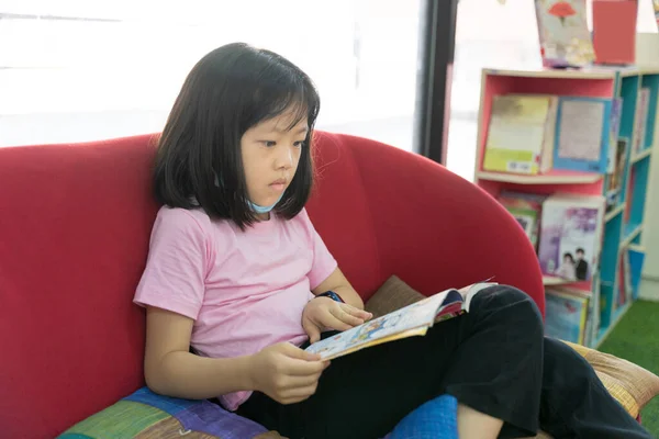Petite Fille Asiatique Lit Livre Tout Étant Assis Près Fenêtre — Photo