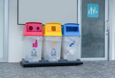 Umumi tuvaletlerin önünde üç renkli geri dönüşüm kutusu. Geri dönüşüm sembollü kutular