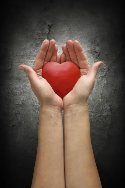 Les mains de la femme tenant le cœur sur un mur de béton sombre — Photo