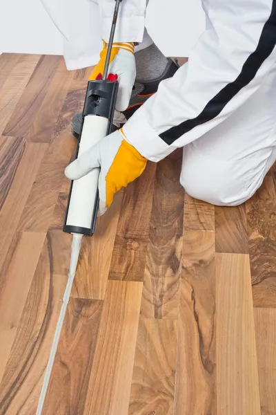 Aplicando selante de silicone em espaços de piso de madeira velha — Fotografia de Stock