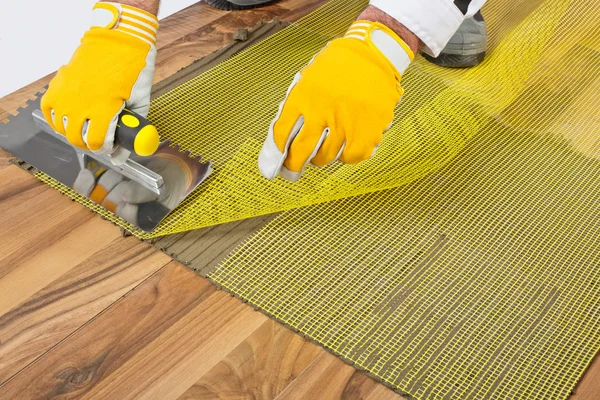 Applicazione di adesivo per piastrelle con rete di rinforzo sul pavimento in legno — Foto Stock