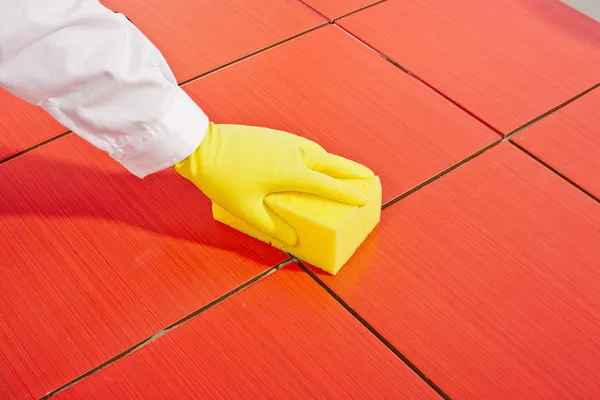 Mano con guantes amarillos y esponja amarilla limpia azulejos rojos — Foto de Stock