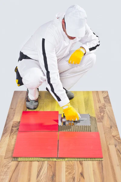 Worker applies ceramic tiles on wooden floor with notched trowel — Stock Photo, Image