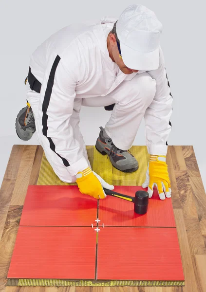 Worker applies ceramic tiles on wooden floor with rubber hammer — Stock Photo, Image