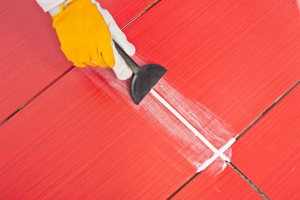 Worker applies grout whit rubber trowel red tiles — Stock Photo, Image