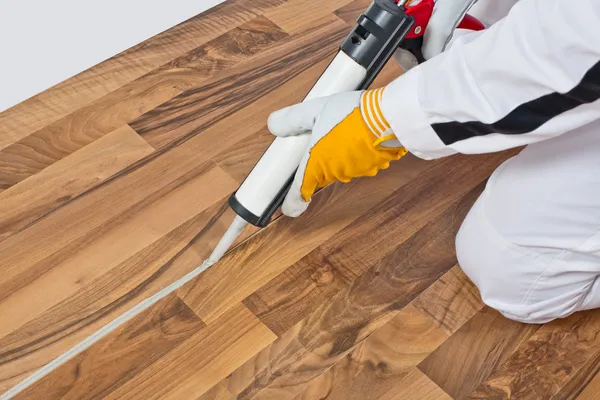 Trabajador aplica espacios de sellador de silicona de piso de madera viejo — Foto de Stock