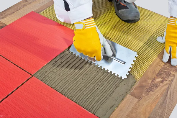 Worker apply ceramic tiles on wooden floor mesh trowel — Stock Photo, Image