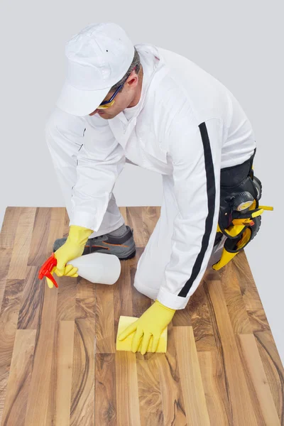 Worker cleans with sponge and spray wooden floor before tilling — Stock Photo, Image