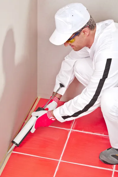 Trabajador en patines blancos pone sellador de silicona esquina piso de la pared — Foto de Stock