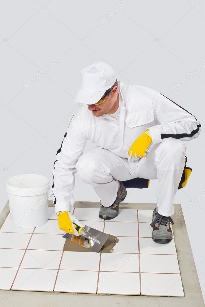 Worker repairs old white tiles with tile adhesive and trowel