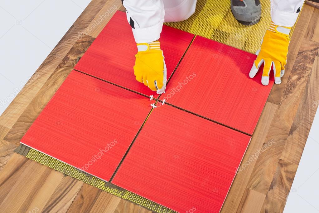 Worker levels crosses Tiles applied on old wooden Floor reinforc