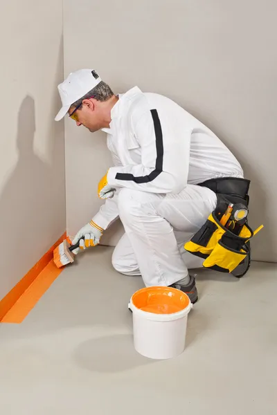 Arbeiter mit Bürstenabdichtung an Wand und Boden Stockbild