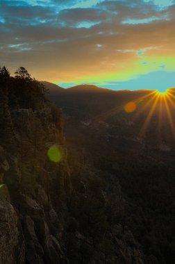 New Mexico 'daki SantaFe Ulusal Ormanı' nda bulutlu bir sabahta güneş ufku aydınlatıyor. Işık ışınları karanlığı delip geçer güneş uzaktaki dağların üzerinden yükselirken