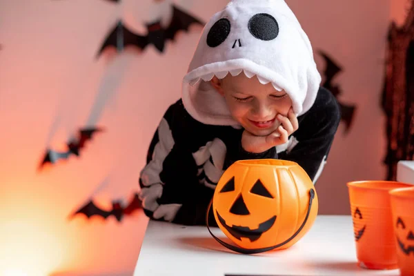 Niño de Halloween con cubos de calabaza en traje de esqueleto comiendo dulces en casa. Listo para engañar o tratar vacaciones —  Fotos de Stock