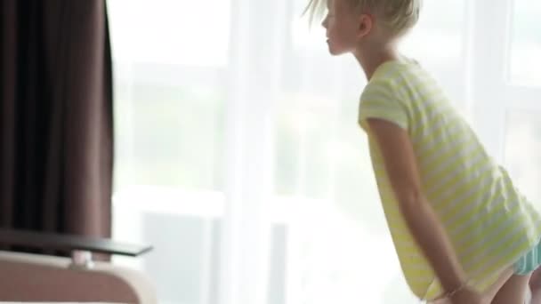 Petite fille blonde souriante qui se couche le matin à la maison. L'enfant agite la couverture pour la répandre. Des draps frais. Les routines quotidiennes — Video