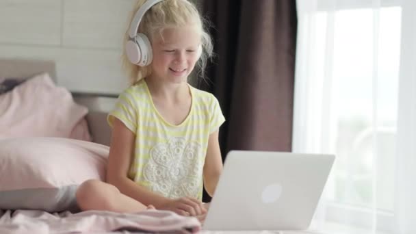 Blonďatá školačka studuje doma v posteli a dělá domácí úkoly s laptopem. Vzdálenost učení on-line vzdělávání. Zpátky do školy — Stock video