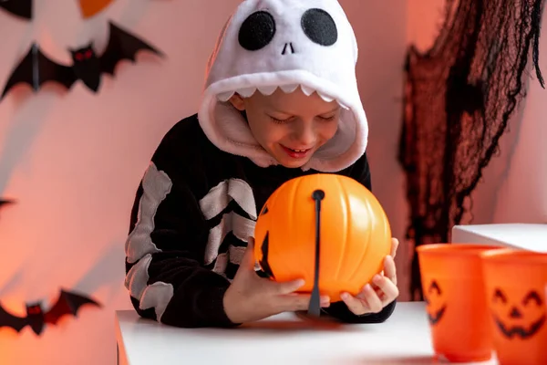 Niño de Halloween con cubos de calabaza en traje de esqueleto comiendo dulces en casa. Listo para engañar o tratar vacaciones —  Fotos de Stock
