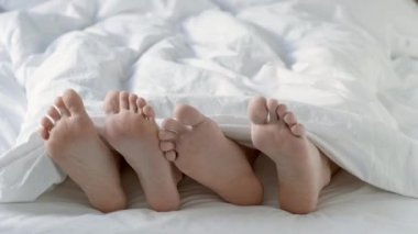 Tutkulu bir çift yatak odasında beyaz bir battaniyenin altında sevişiyor..