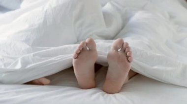 Tutkulu bir çift yatak odasında beyaz bir battaniyenin altında sevişiyor..