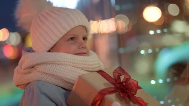 Portrait Boy with Gifts box looking and dreaming in Christmas window shopping on traditional Christmas market. Xmas Presents Holidays childhood concept. — Stock Video