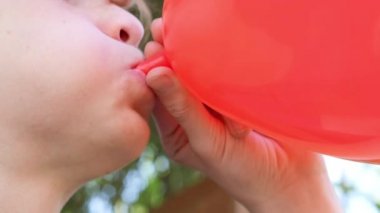 Genç çocuk hava balonu şişiriyor. Kırmızı kalp şeklinde balon tutan kızıl saçlı yakışıklı çocuk ellerinde balon tutuyor. Ağız kapanışı. Mutlu yıllar, mutlu yıllar, mutlu yıllar.