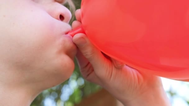 Genç çocuk hava balonu şişiriyor. Kırmızı kalp şeklinde balon tutan kızıl saçlı yakışıklı çocuk ellerinde balon tutuyor. Ağız kapanışı. Mutlu yıllar, mutlu yıllar, mutlu yıllar. — Stok video