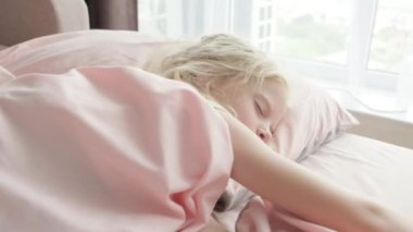 Sevimli sarışın kız sabahları evdeki pembe çarşafların üzerinde tatlı tatlı uyuyor. Çocuk hayalleri, rahatlık, huzur ve huzur.